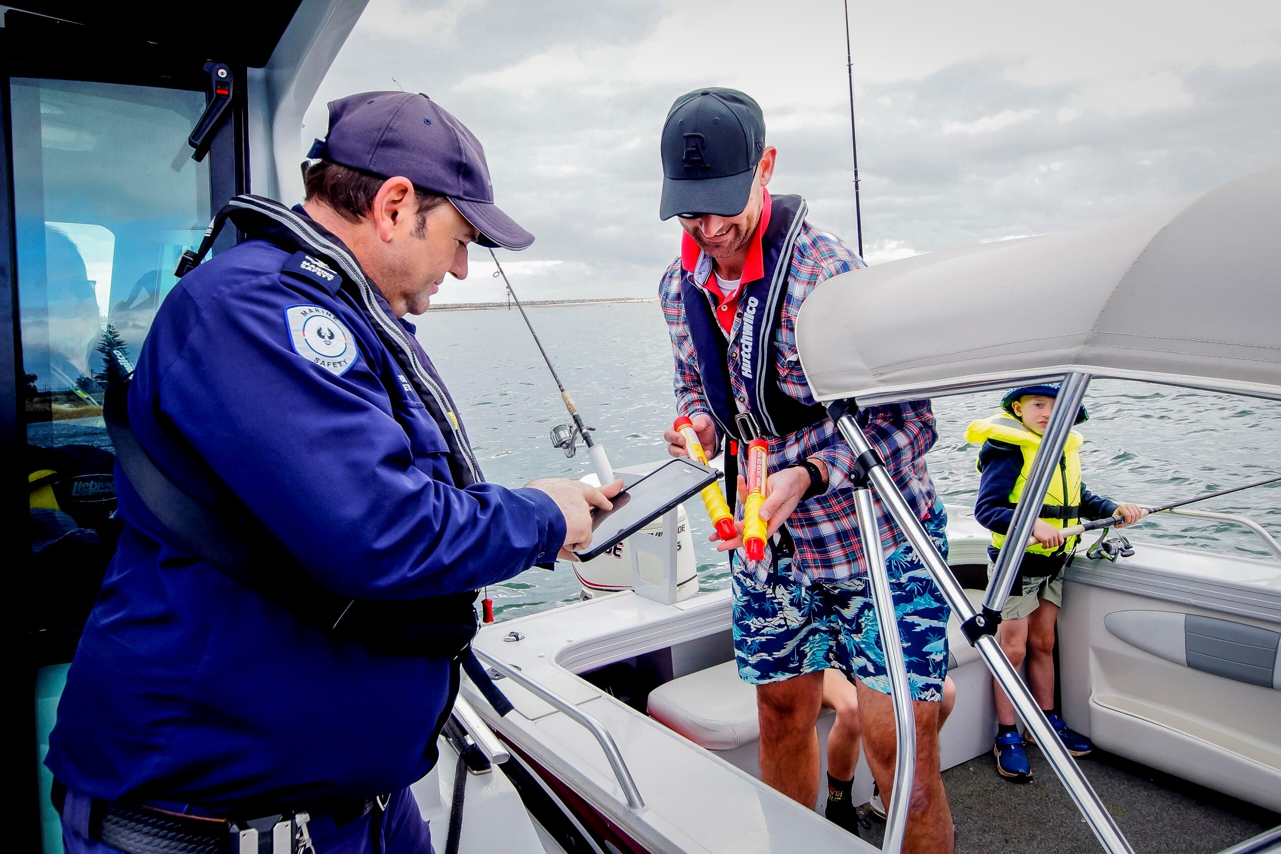 Pictured is a Marine Safety Officer checking to see if a boater on the water has his flares in date. Marine Safety Officer is checkig the flares while boarded on the Marine Safety Vessel with the boater aboard his own vessel with a child (son) just behind him.