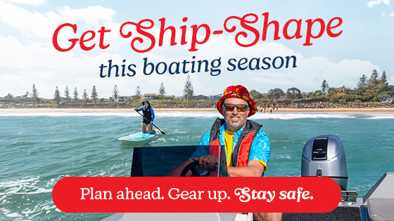 Man operating a boat on ocean waters with paddleboarder in the background with the words Get Ship Shape this boating season - Plan ahead. Gear Up. Stay Safe