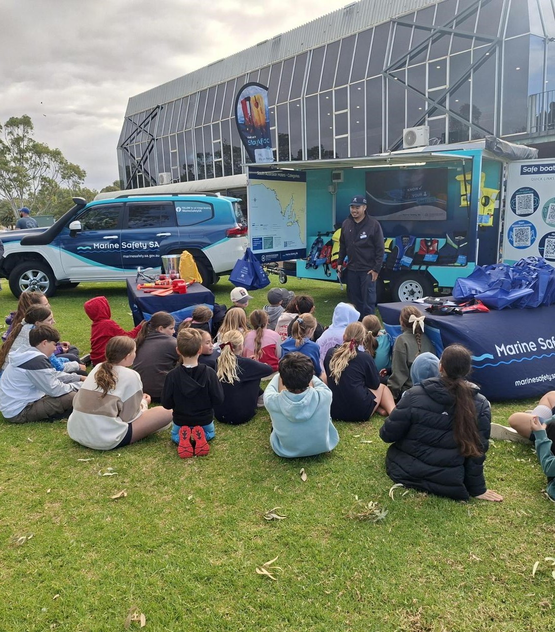 Pictured is one of our Marine Safety Officers sharing important boating safety tips to children at the Surf Life Saving SA's little Rippers program at Murray Bridge. The children are all sitting on the grass listening.