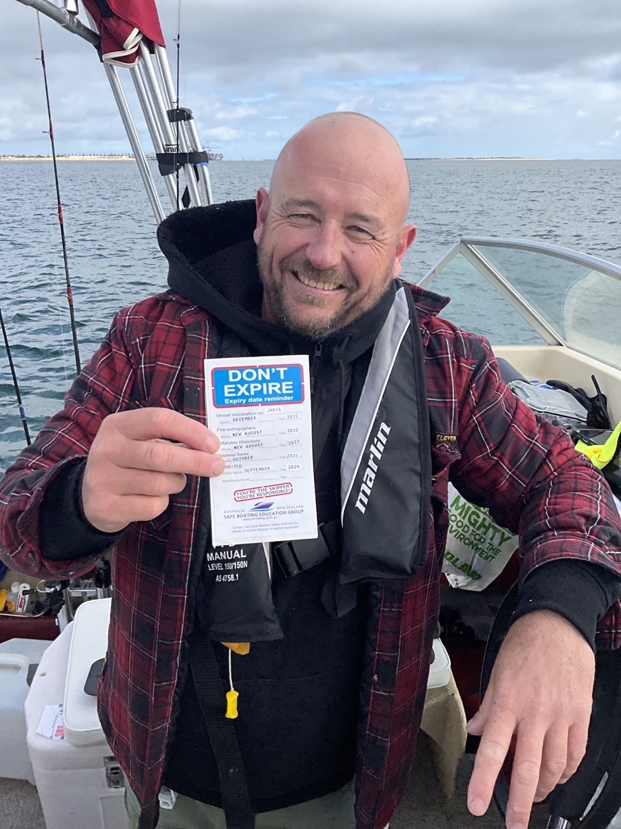 A gentleman in his vessel out on the ocean with a big smile holding a don't expire sticker