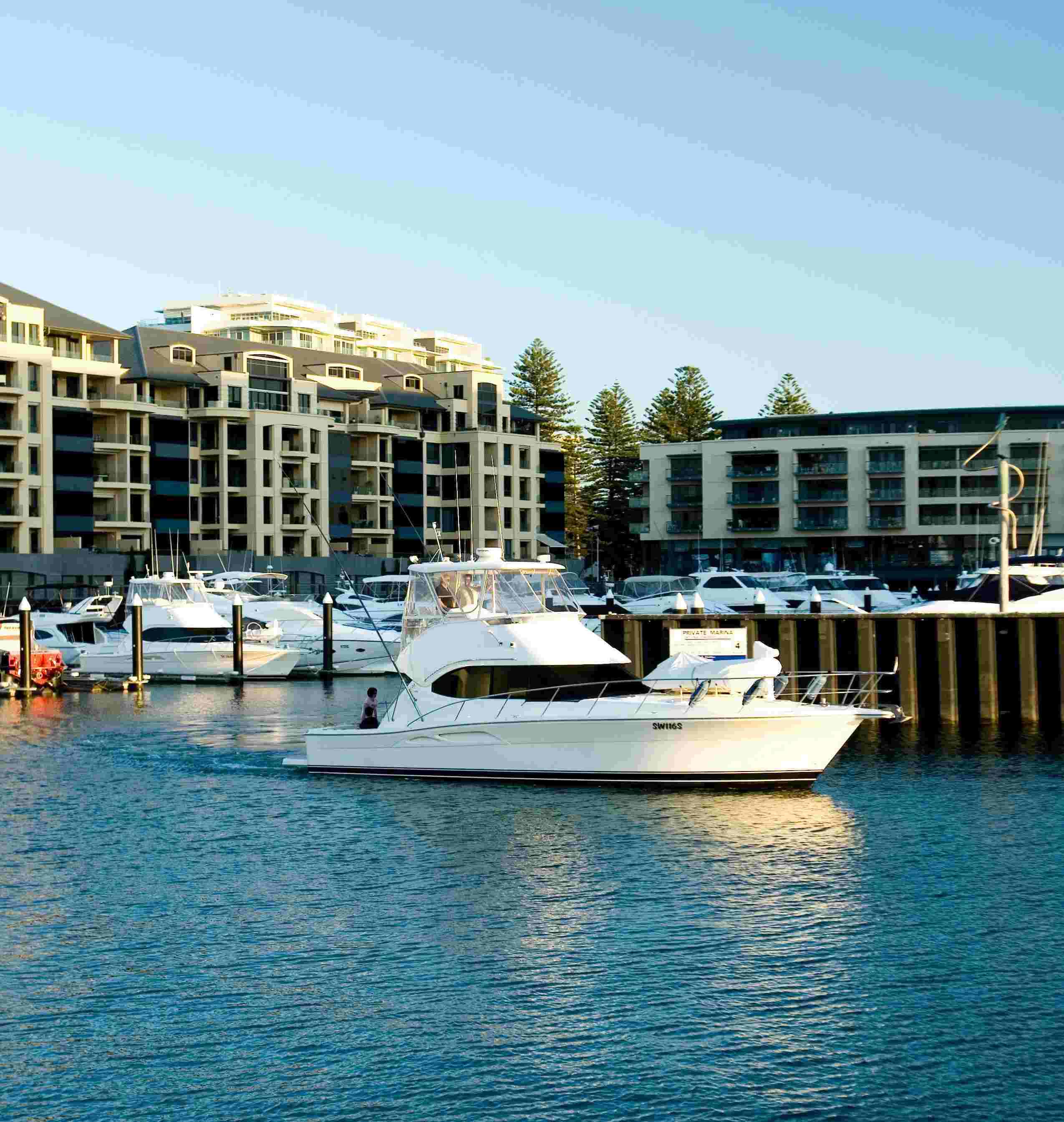 Cruising boat on the water at Holdfast Bay marina with boats and apartment buildings in the background