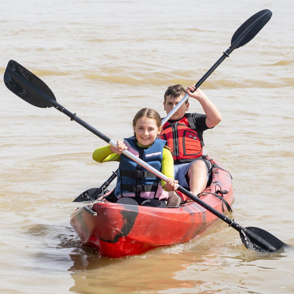 Two children kayaking on calm water while wearing properly fitted lifejackets.