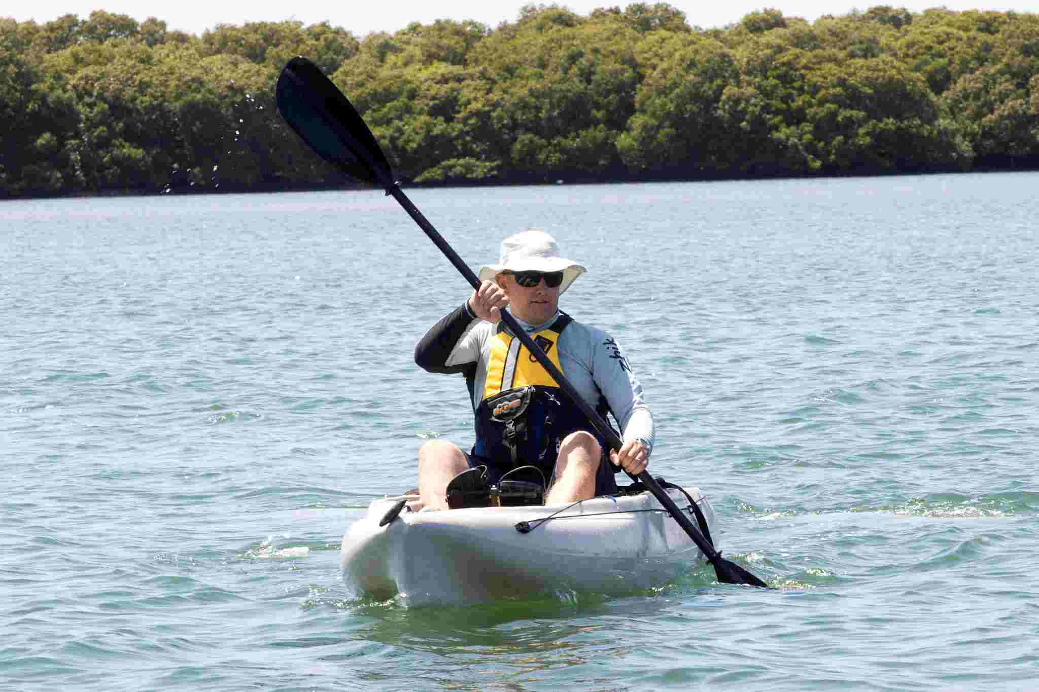 Man paddling on a kayak with a lifejacket on and mangroves showing in the background