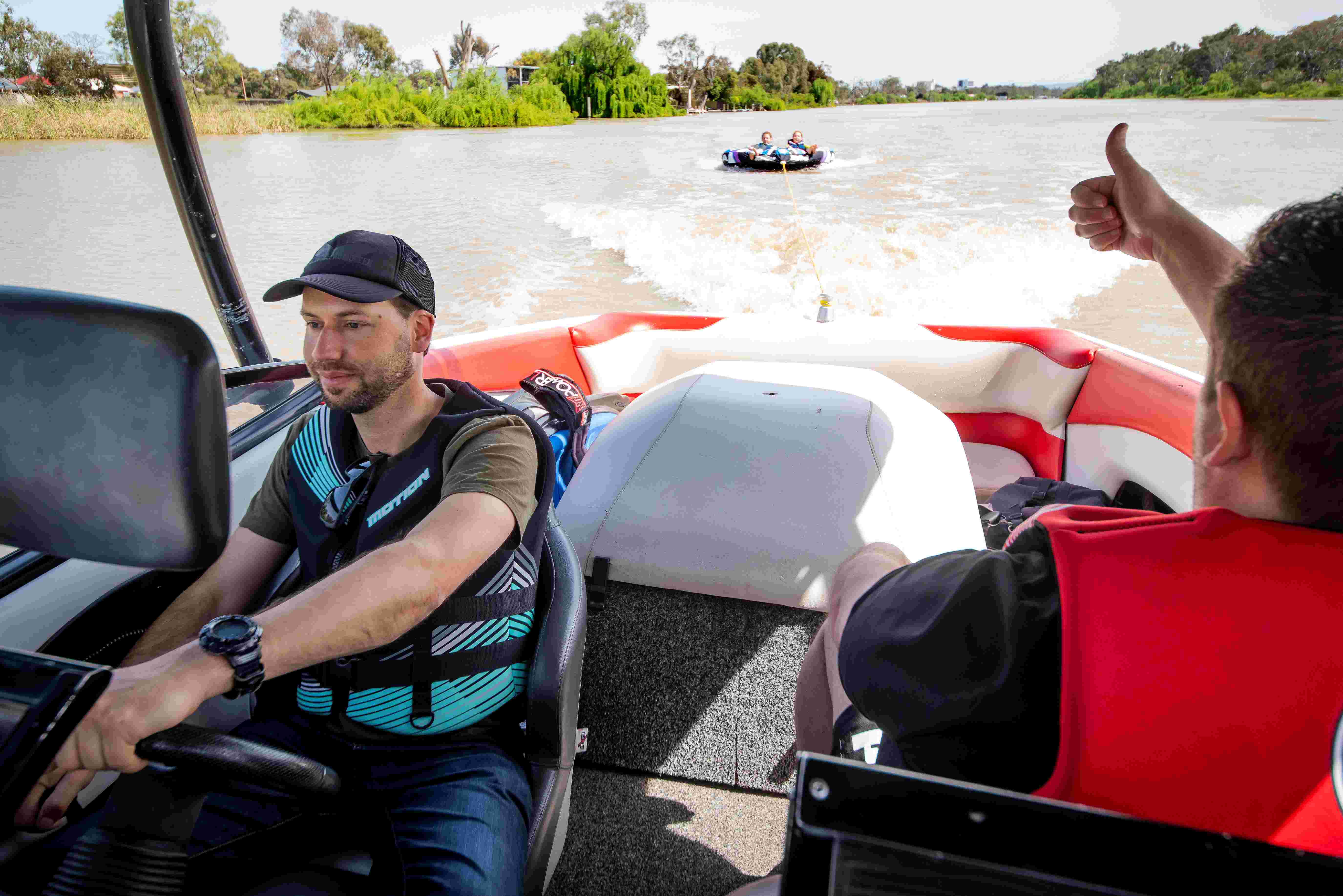 Picture taken up on the River Murray with two people on a ski boat pulling to people on an inflatable water tube