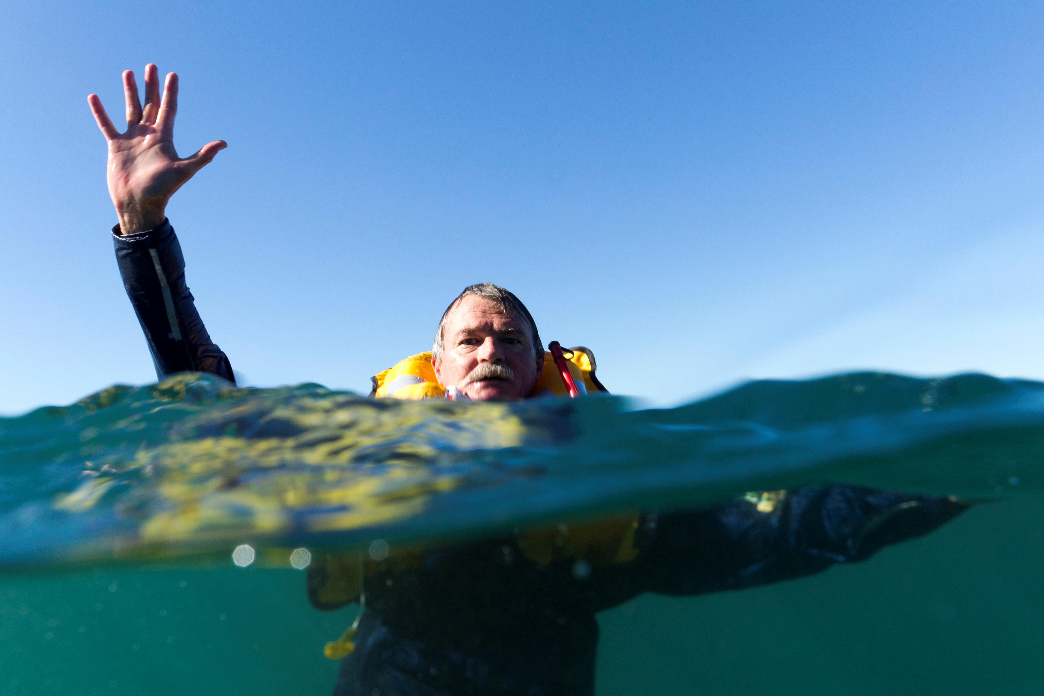 A gentleman in a lifejacket in the water with his hand up in the air requesting help