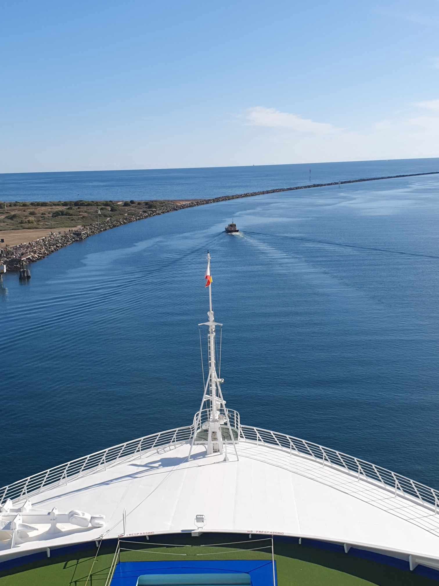 View from the bow of a cruise ship heading out to sea at outer Harbor with a pilot boat shown in the distance