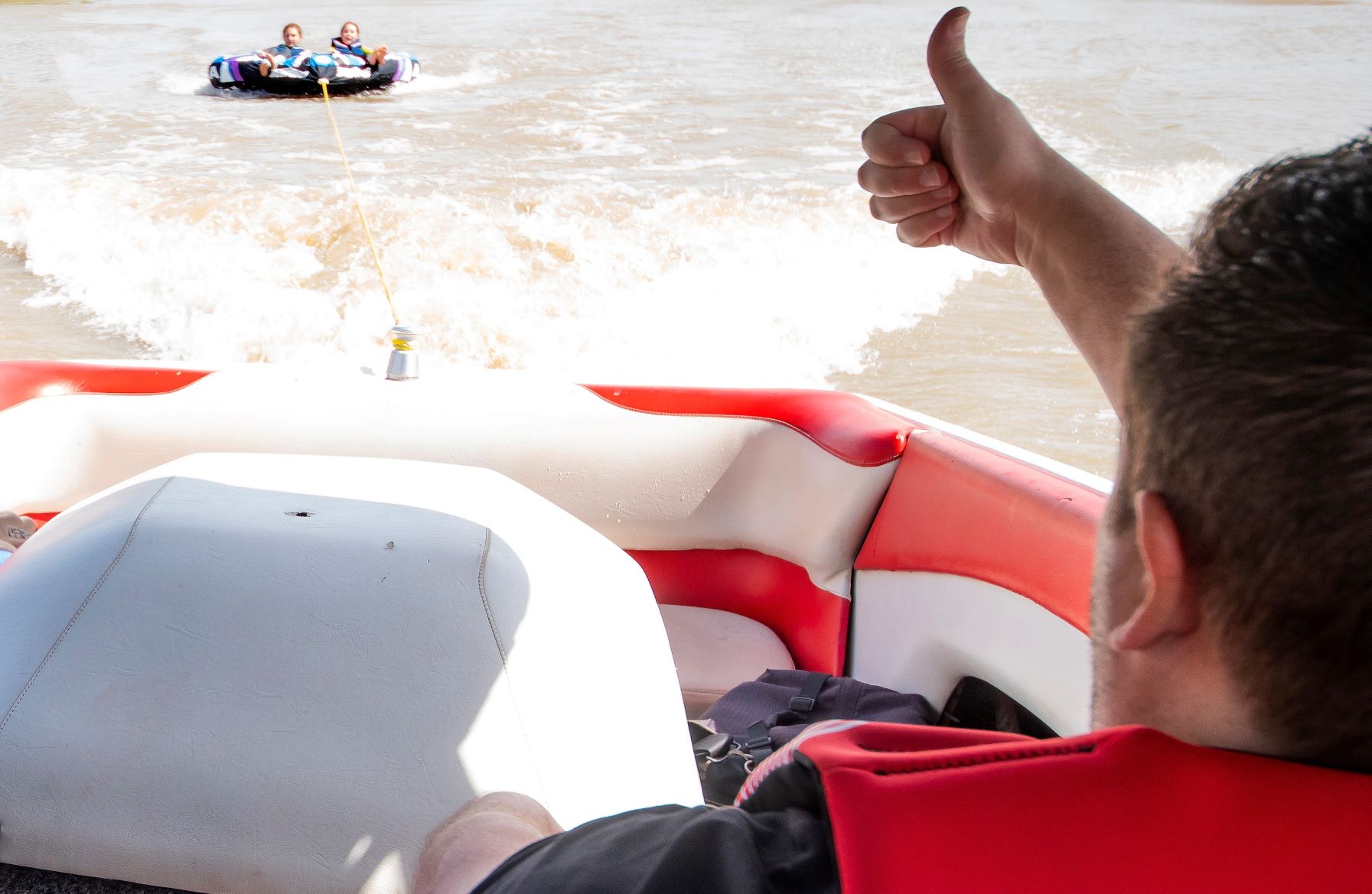 Man in boat giving thumbs up to children being towed on a tube